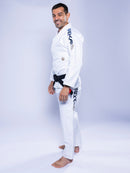 A man wearing the SEKAI 3.0 BJJ Gi White Navy with dark lettering on the sleeve and pants stands barefoot on a white background, smiling and looking at the camera.