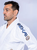 A man with short dark hair and a trimmed beard wears the white-navy SEKAI 3.0 BJJ Gi, embroidered with "SEKAI" on the shoulder, looking left against a plain light background.
