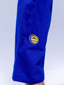 A close-up of someone wearing the SEKAI 3.0 BJJ Gi Blue Yellow, featuring a yellow circular mountain patch on the upper leg. The background is light and uncluttered.