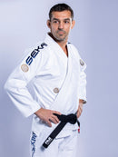 A man stands confidently with his hands on his hips, wearing the SEKAI 3.0 BJJ Gi White Navy and a black belt, looking to the side against a plain light background.